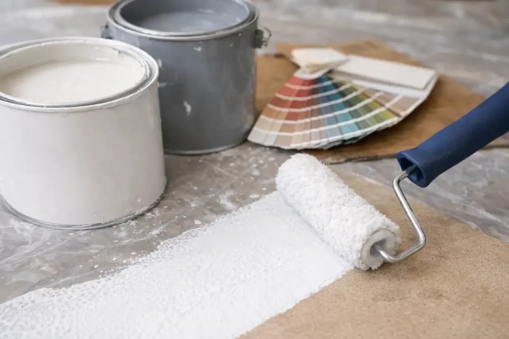 Gros plan d’un rouleau microfibre appliquant une peinture blanche, avec deux pots de peinture ouverts et un nuancier en arrière-plan.