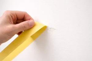 Main retirant un ruban de masquage, peinture arrachée sur un mur clair