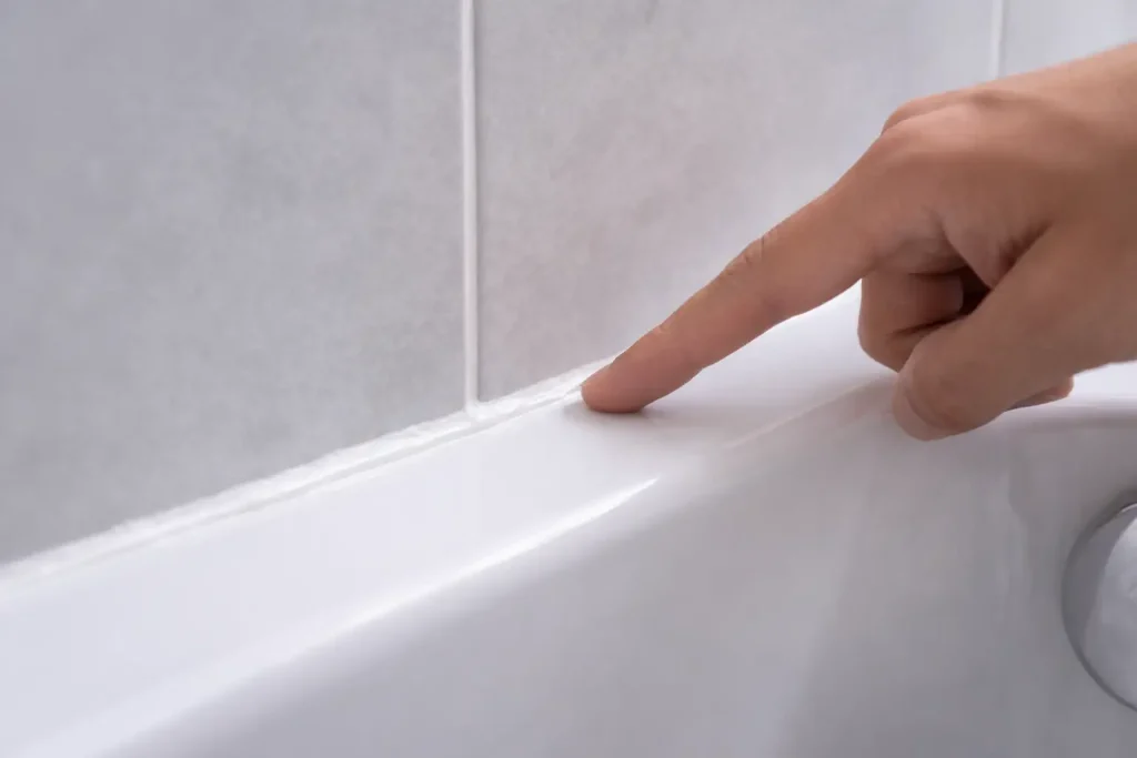 Main montrant un joint silicone encore frais dans un angle de salle de bain