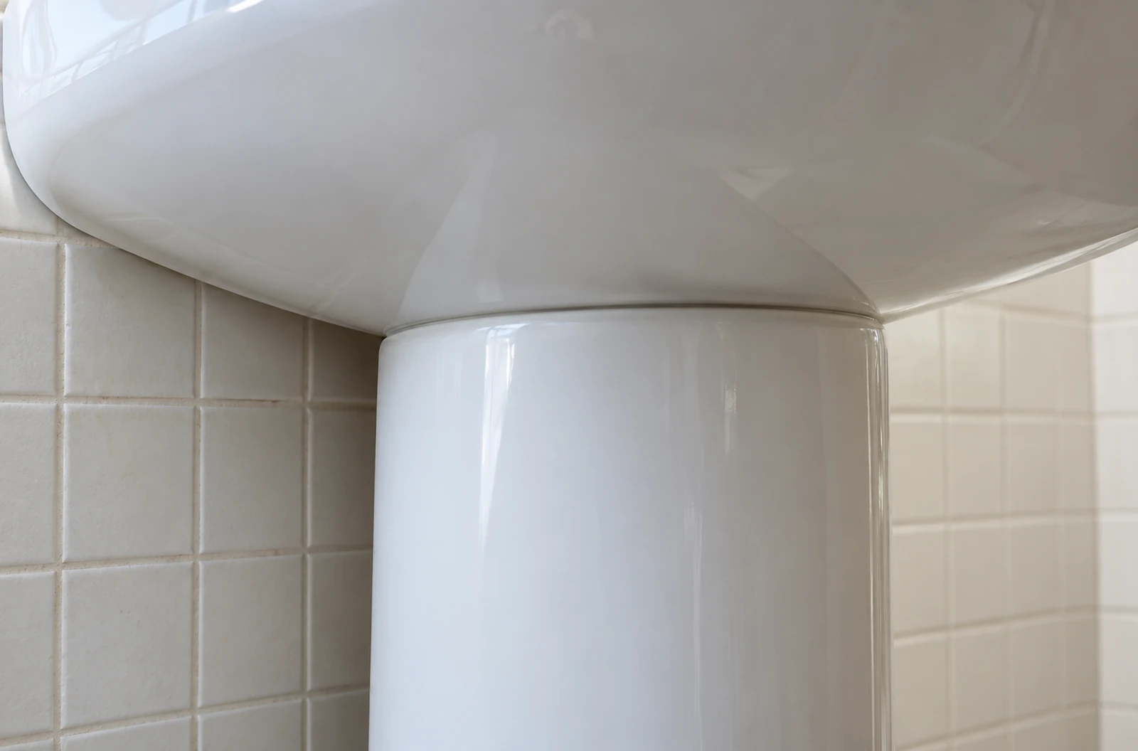 Jonction entre le dessous d’un lavabo blanc et le haut de sa colonne en céramique