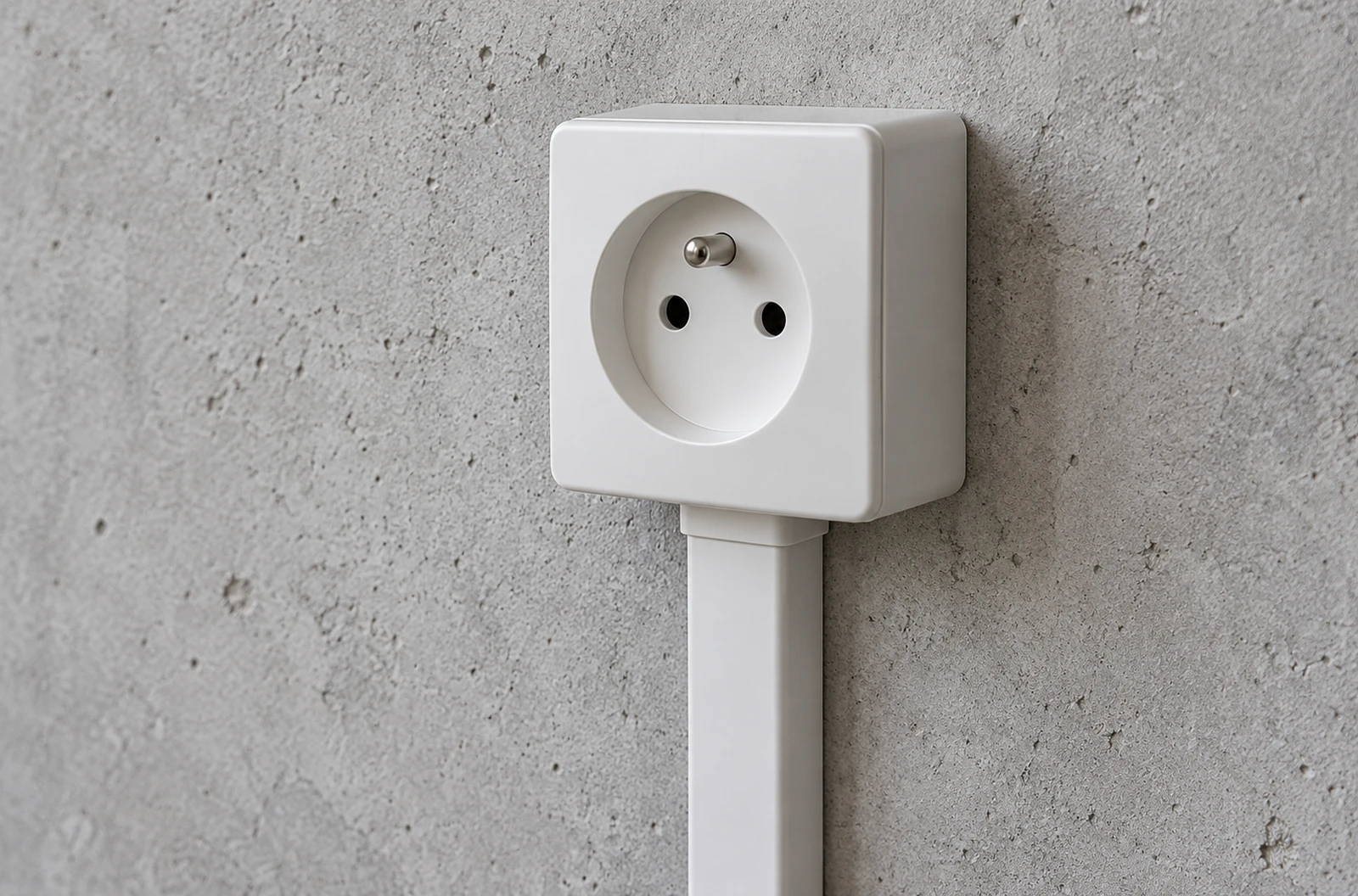 Prise blanche en saillie sur un mur en béton avec une moulure fermée arrivant sous le boîtier
