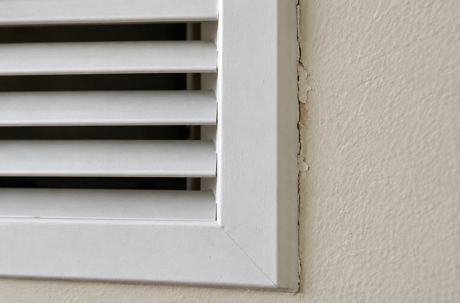 Détail d’une grille blanche ouverte avec un raccord de peinture abîmé sur le bord du cadre